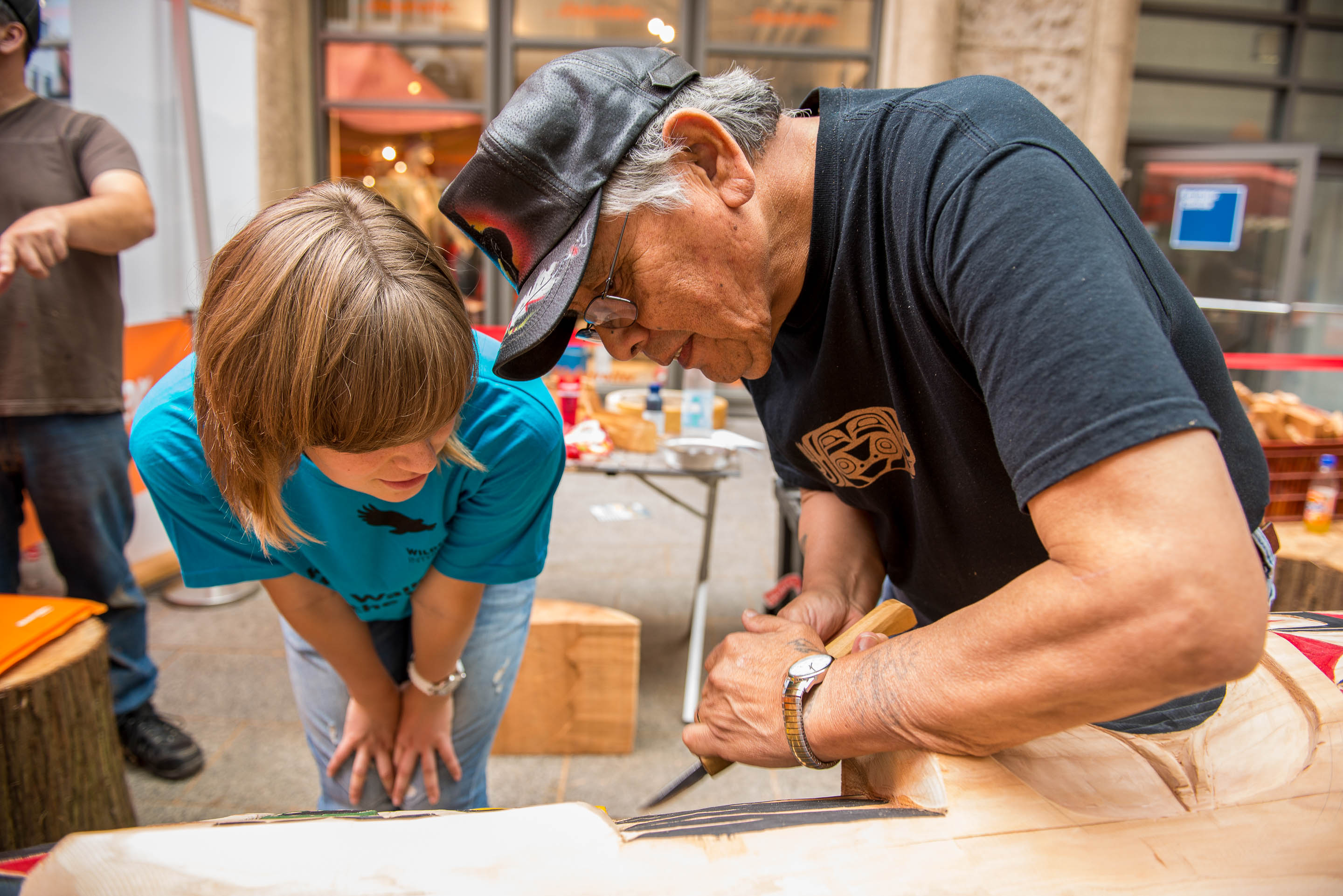 Harald Joe ein Indigener Schnitzer der Cowichan aus Kanada zeigt einer Schuelerin wie er den Totempfahl schnitzt. 